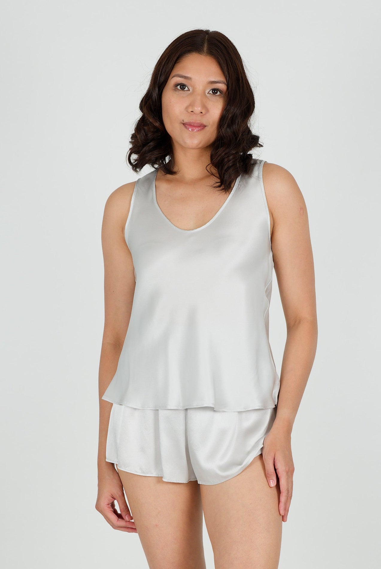 Woman wearing a silk silver tank top and shorts on a white background