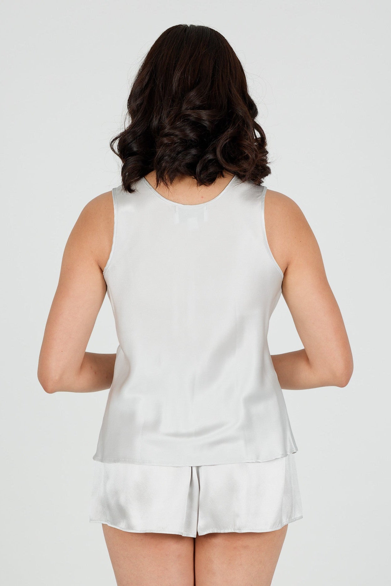 Person wearing a silver silk sleeveless top and shorts on a plain background