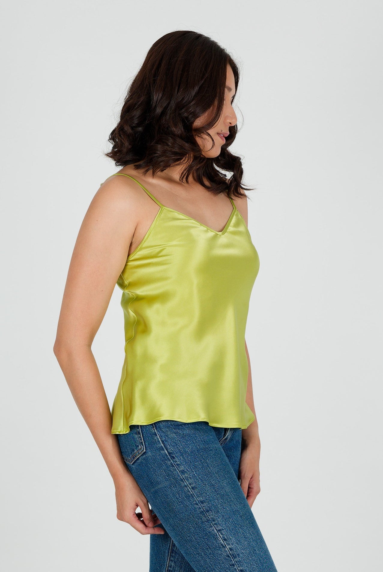 Woman wearing a green silk satin camisole top and blue jeans on a white background