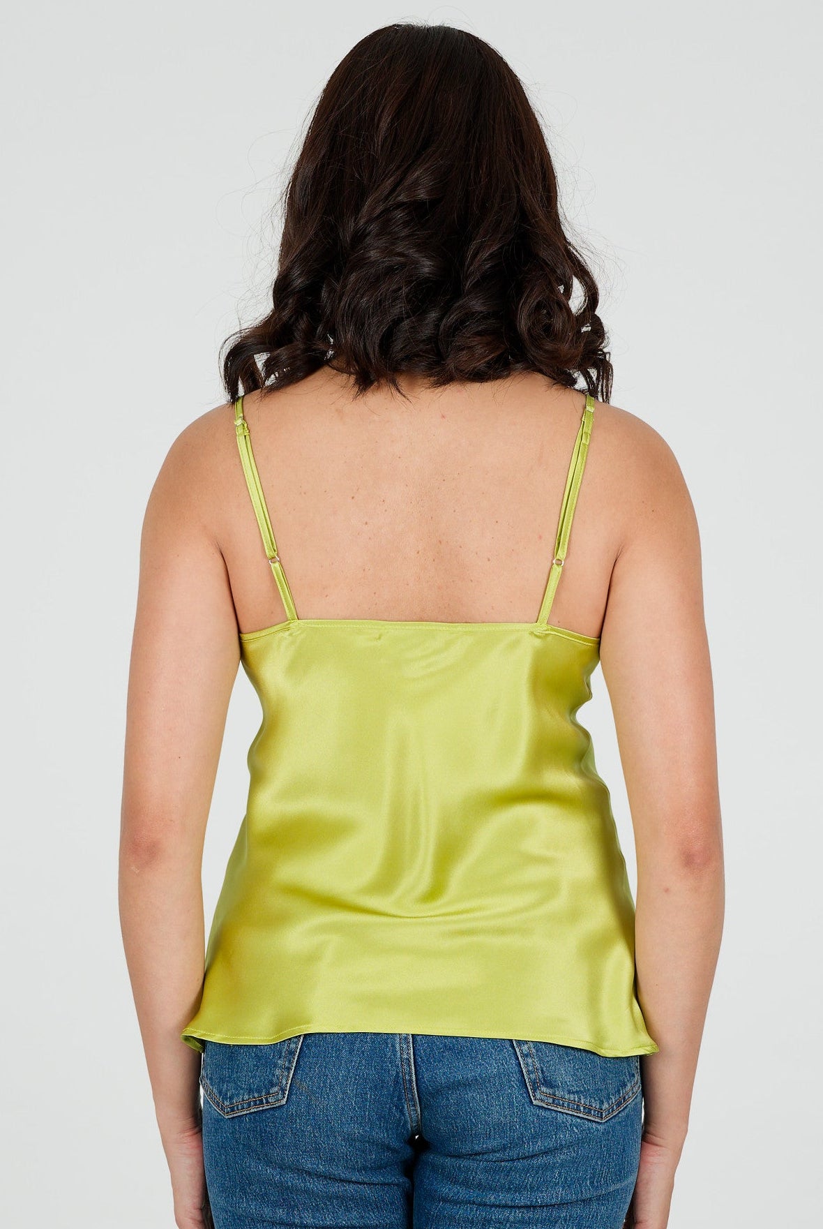 Person wearing a green silk camisole top and blue jeans on a white background