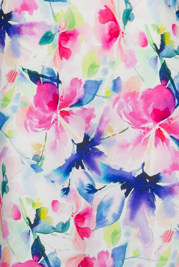 A woman wearing a floral silk chemise slip with vibrant hues of fuchsia pink, soft blue, and fresh green.