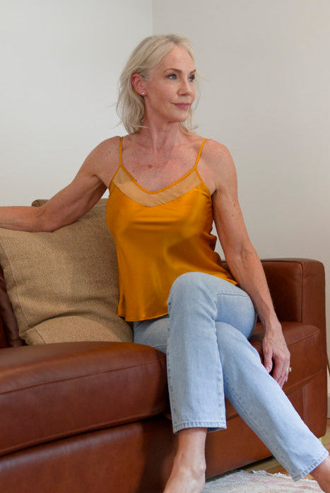 Woman in a bronze silk camisole top sitting on a brown couch