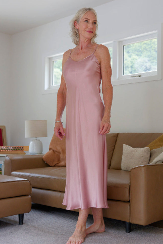 Woman in a pink silk satin slip dress nightie standing in a living room