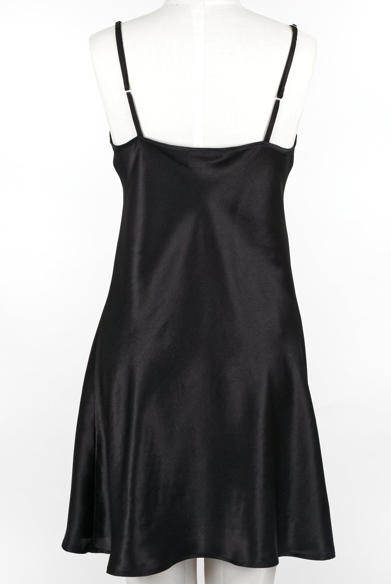A woman wearing a black silk chemise slip that reaches mid-thigh, with thin adjustable straps and a V-neckline
