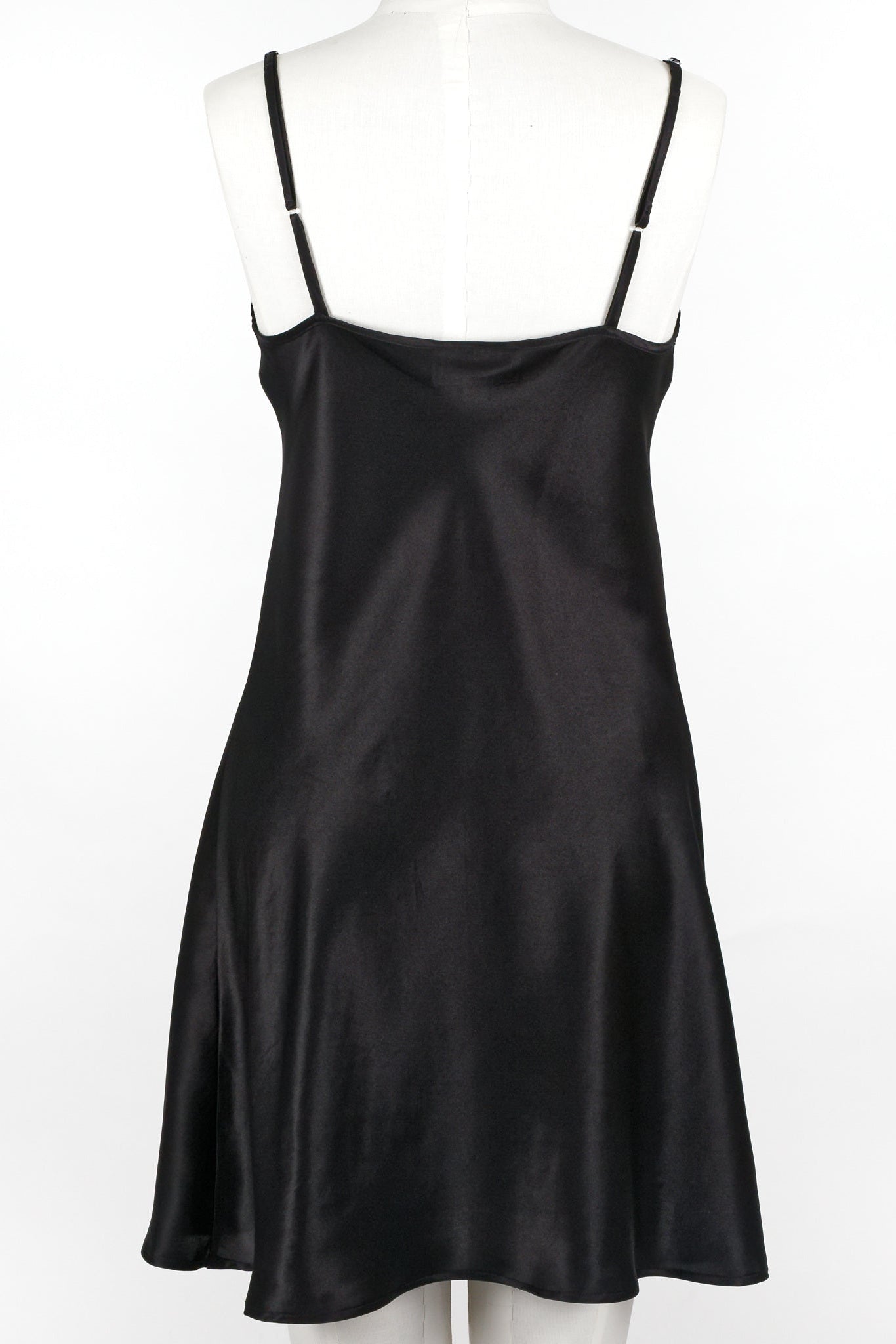A woman wearing a black silk chemise slip that reaches mid-thigh, with thin adjustable straps and a V-neckline