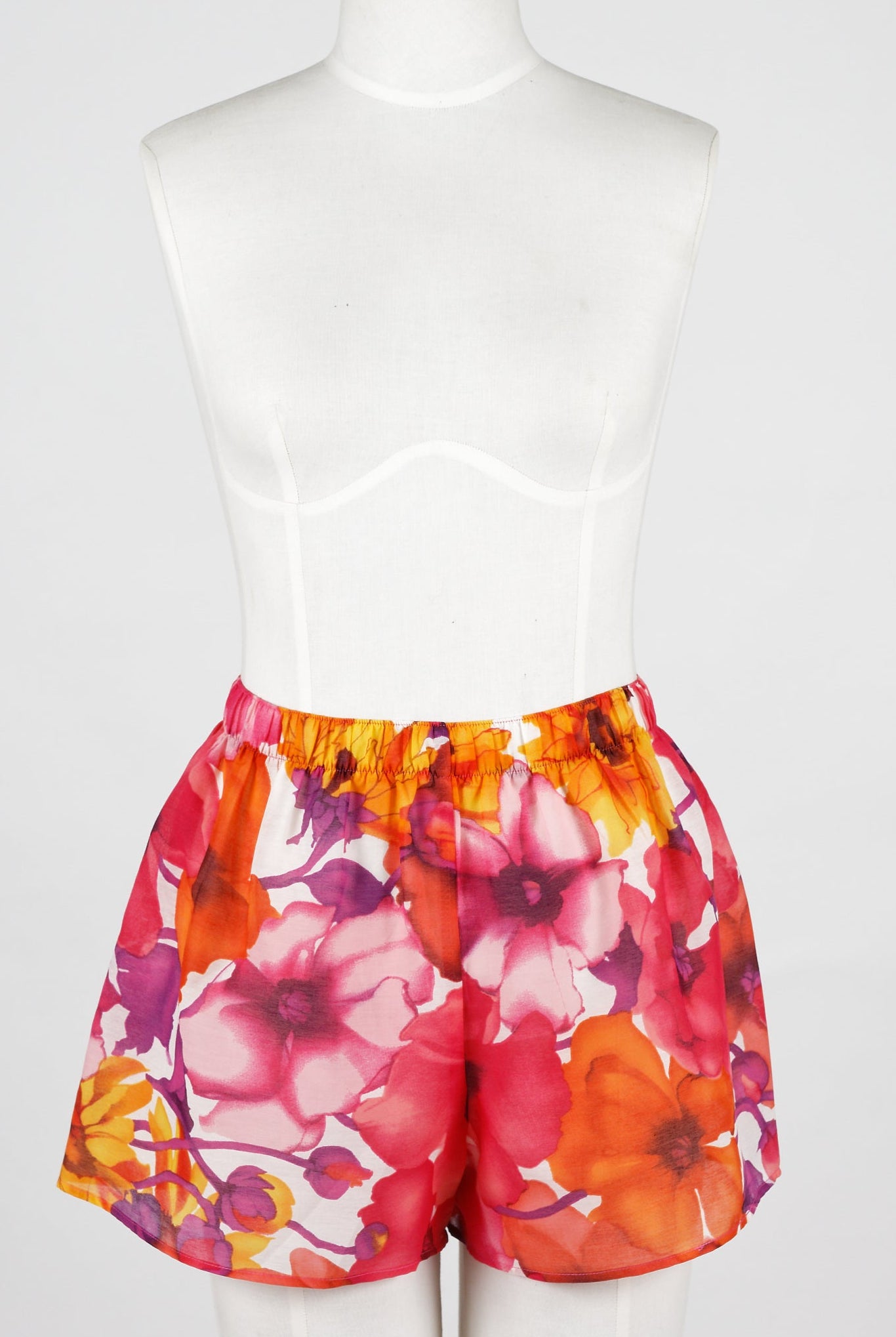 A woman wearing lounge shorts with a bright floral pattern. The shorts have an elastic waistband and she is holding a drink.