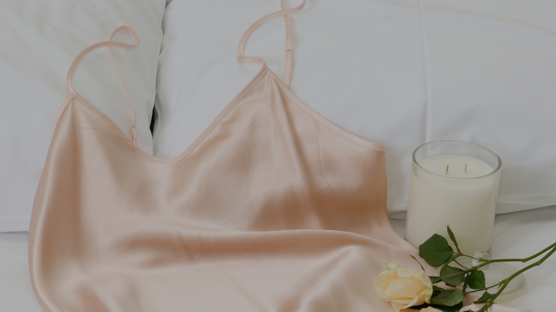 light pink silk camisole top draped on bed with roses and candle