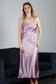 Woman wearing a purple silk satin slip dress standing in front of a gray sofa.