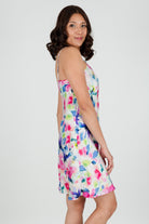 A woman wearing a floral silk chemise slip with vibrant hues of fuchsia pink, soft blue, and fresh green.