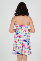 A woman wearing a floral silk chemise slip with vibrant hues of fuchsia pink, soft blue, and fresh green.