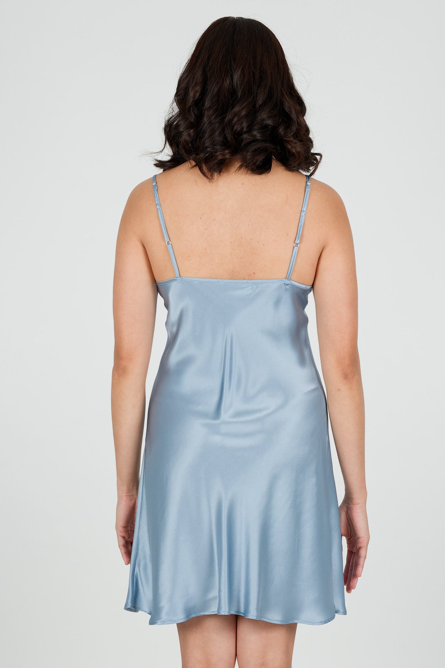 Woman wearing a light blue silk satin slip dress on a white background