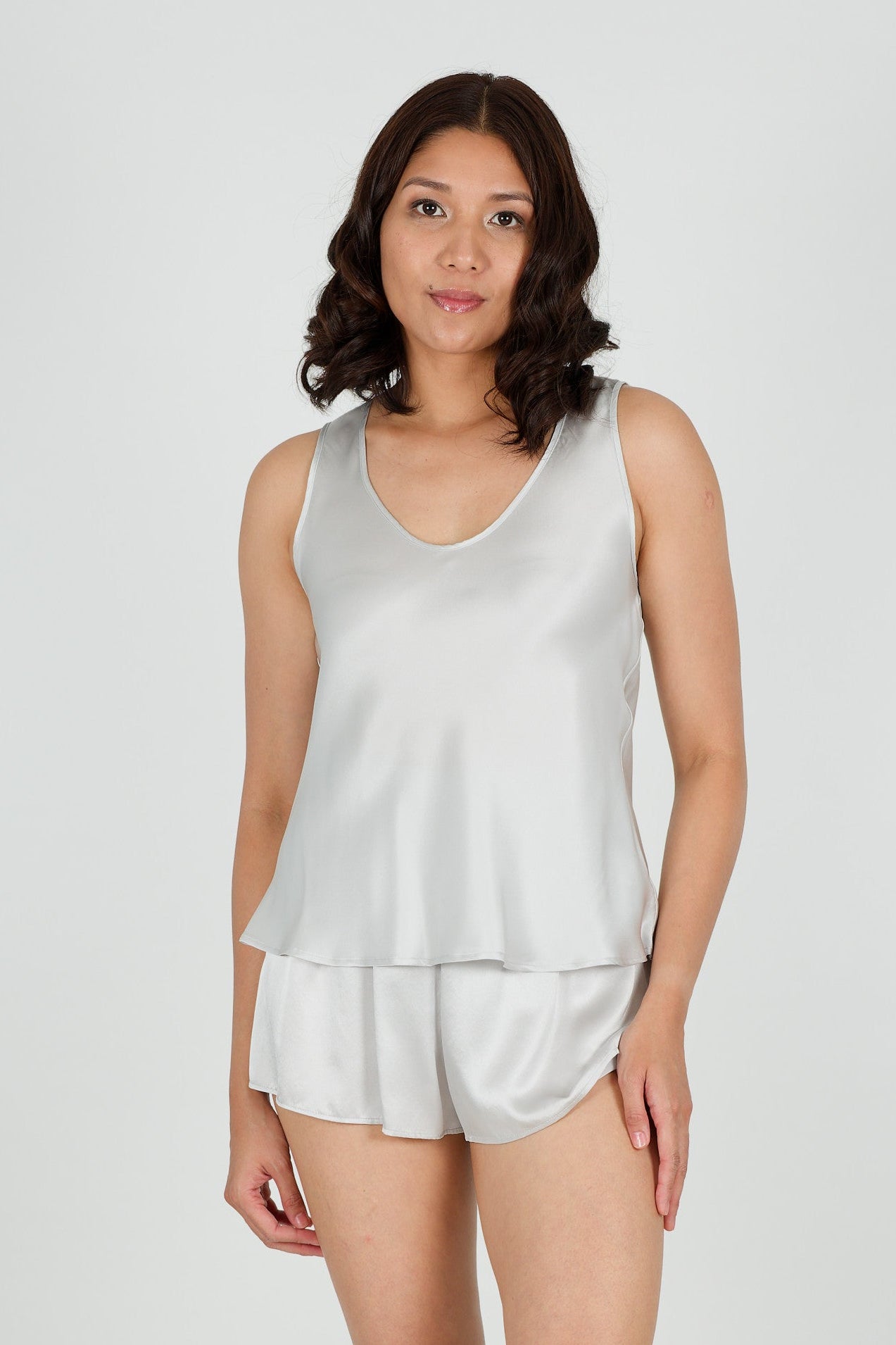 Woman wearing a silk silver tank top and shorts on a white background