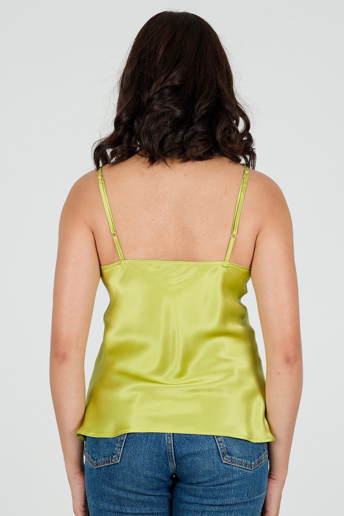 Person wearing a green silk camisole top and blue jeans on a white background