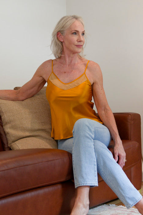 Woman in a bronze silk camisole top sitting on a brown couch 