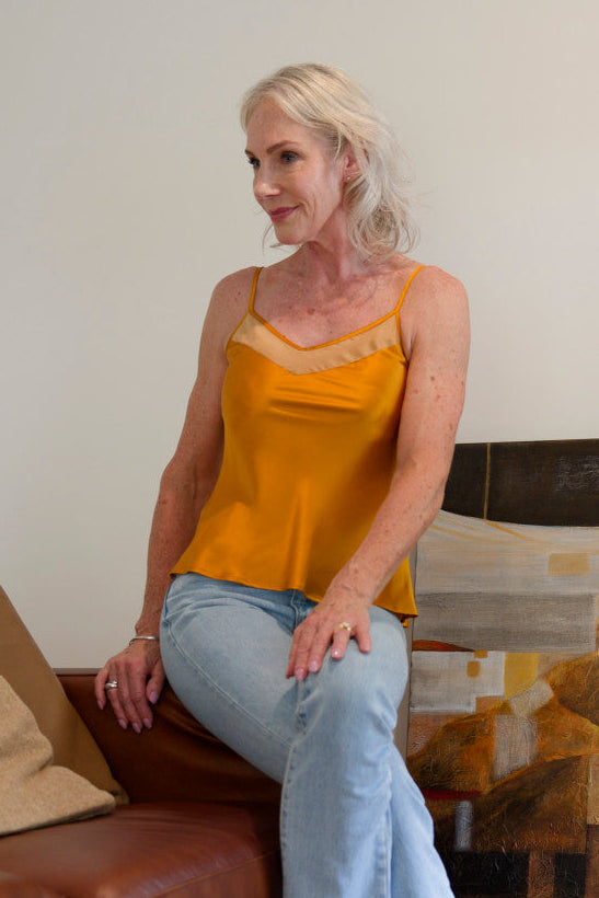Woman in a bronze silk camisole top sitting on a brown couch 