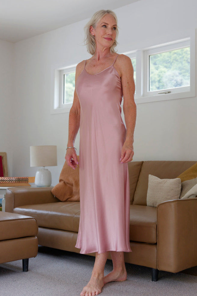 Woman in a pink silk satin slip dress nightie standing in a living room 