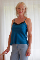 Woman wearing a blue satin silk camisole with black lace trim and jeans