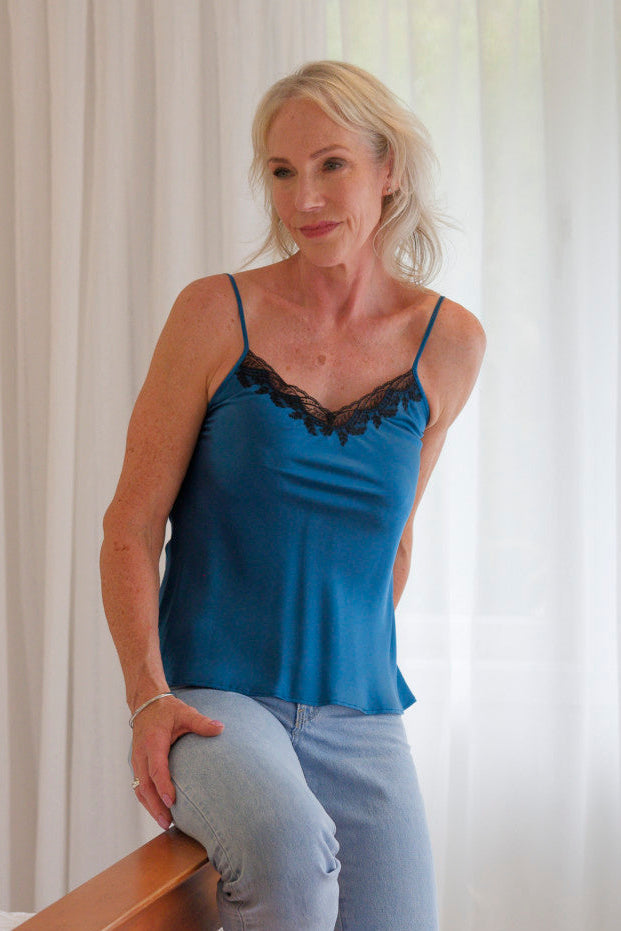 Woman wearing a blue satin silk camisole with black lace trim and jeans