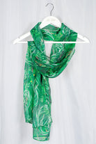 Green patterned silk chiffon scarf on a hanger against a light gray background