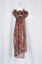 red earthy silk chiffon scarf on a hanger against a plain background
