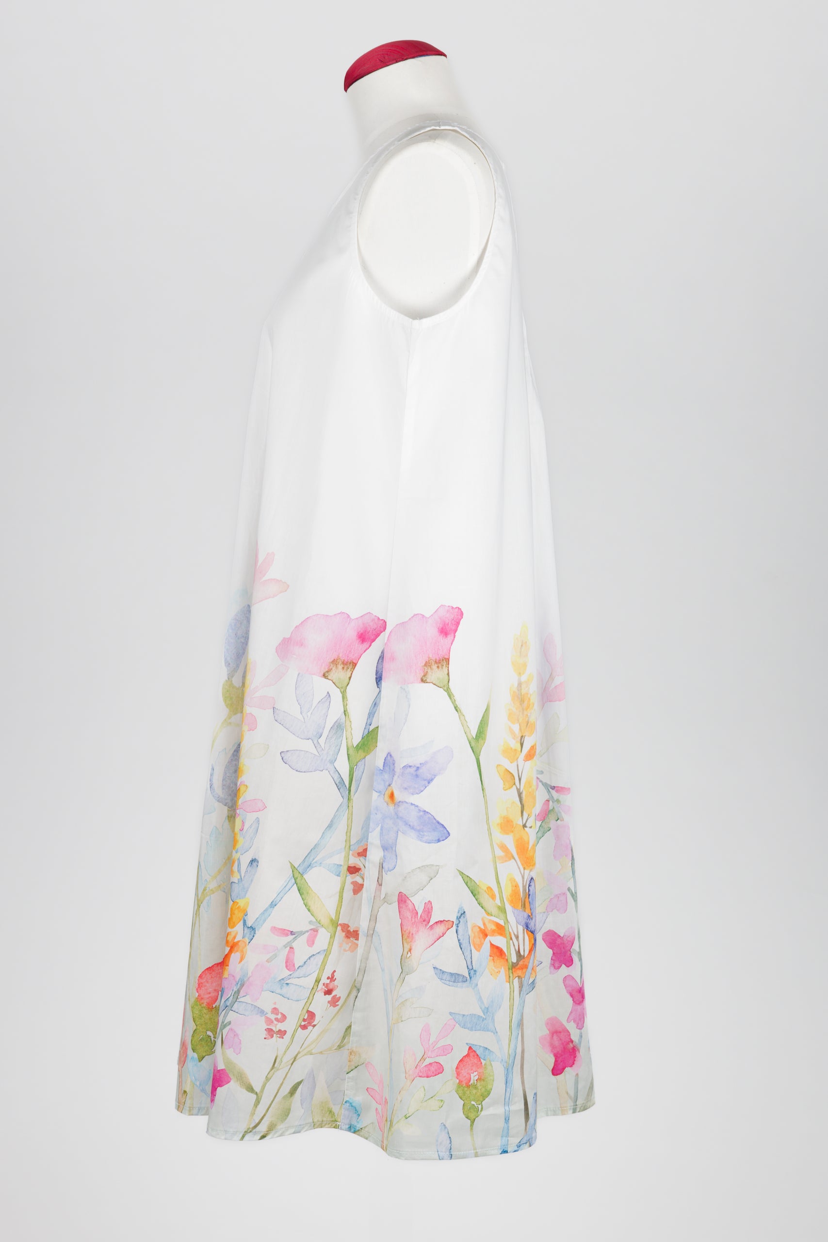 A sleeveless white nightdress displayed on a mannequin against a light gray background, featuring a watercolor floral print concentrated along the lower half with pink, blue, yellow, and green botanical details.