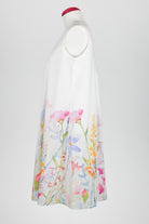 A sleeveless white nightdress displayed on a mannequin against a light gray background, featuring a watercolor floral print concentrated along the lower half with pink, blue, yellow, and green botanical details.