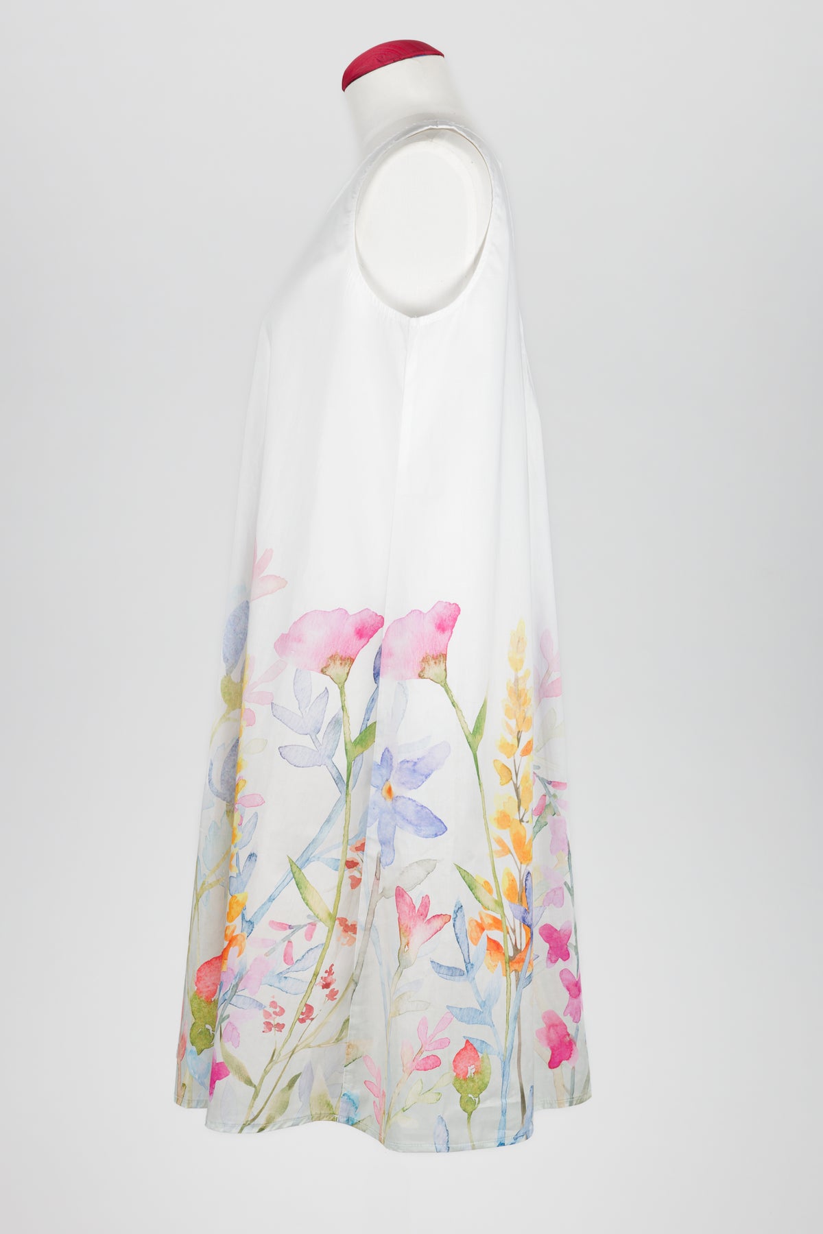 A sleeveless white nightdress displayed on a mannequin against a light gray background, featuring a watercolor floral print concentrated along the lower half with pink, blue, yellow, and green botanical details.