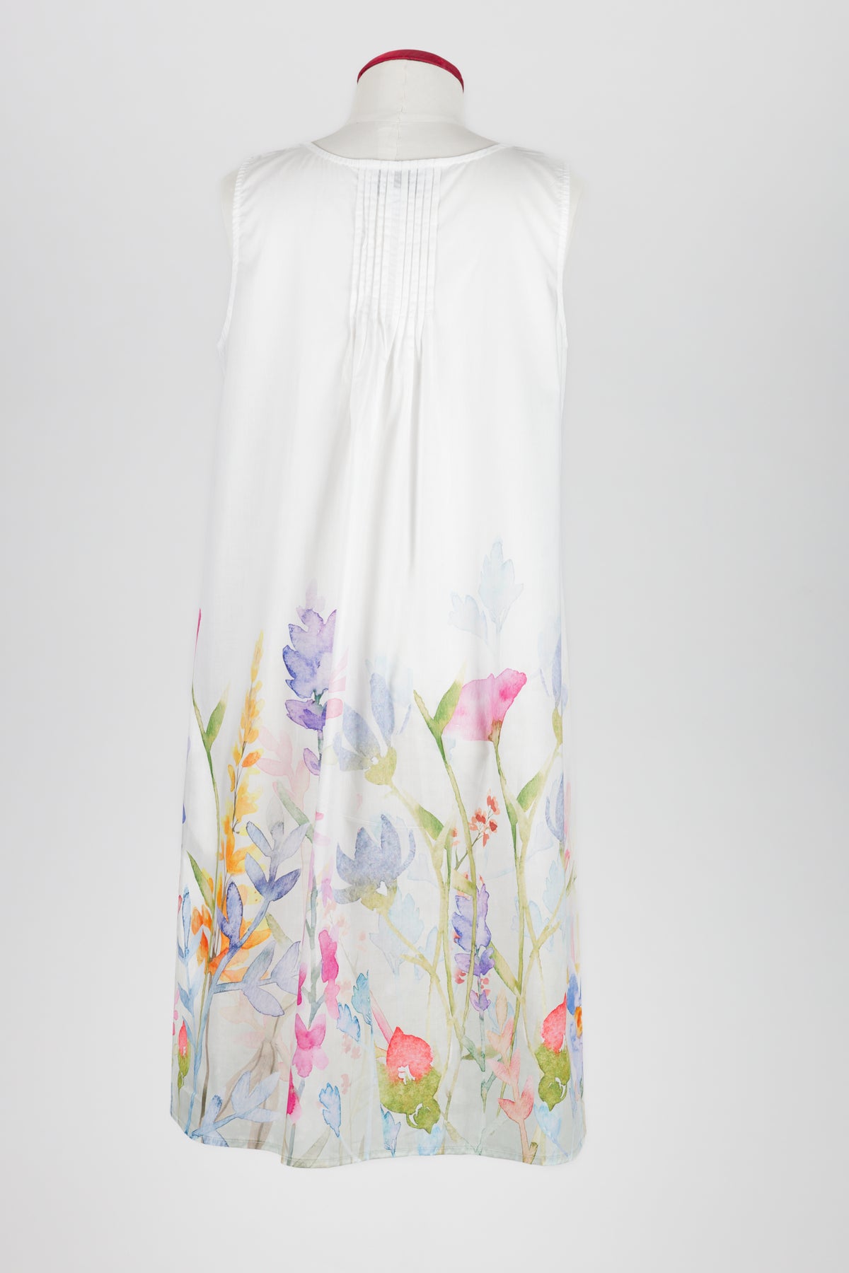 A sleeveless white nightdress displayed on a mannequin against a light gray background, featuring a watercolor floral print concentrated along the lower hem.