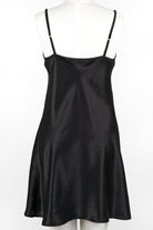A woman wearing a black silk chemise slip that reaches mid-thigh, with thin adjustable straps and a V-neckline