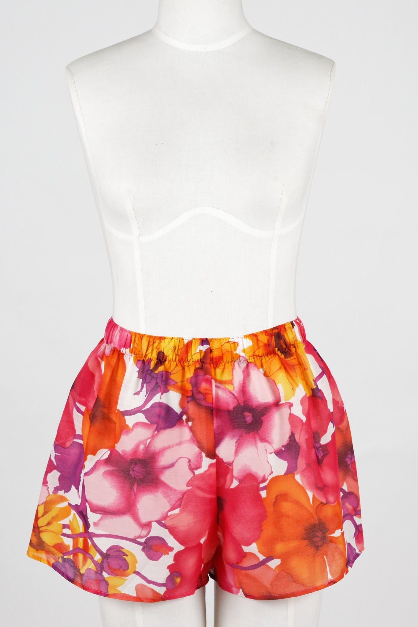 A woman wearing lounge shorts with a bright floral pattern. The shorts have an elastic waistband and she is holding a drink.